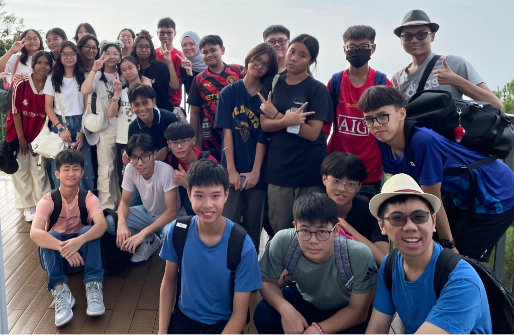 Group photo of smiley students and teachers touring Penang site.